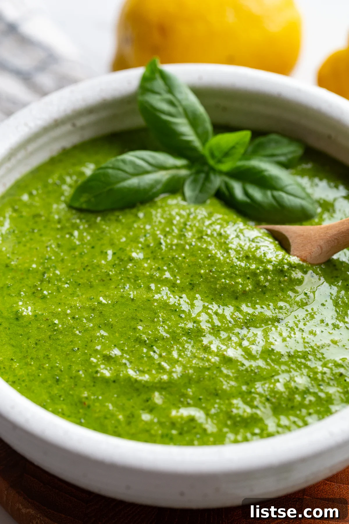Homemade Walnut Pesto Recipe 5 Close-up of walnut pesto in a white bowl garnished with basil, with lemons blurred in the background