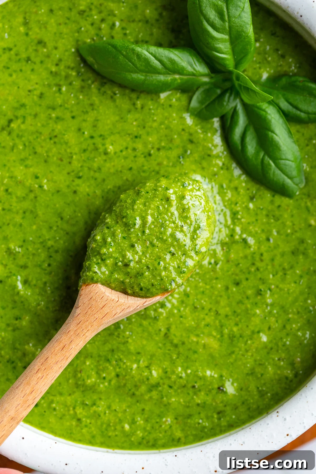 Homemade Walnut Pesto Recipe 9 Close-up of a wooden spoon scooping thick walnut pesto from a bowl garnished with fresh basil