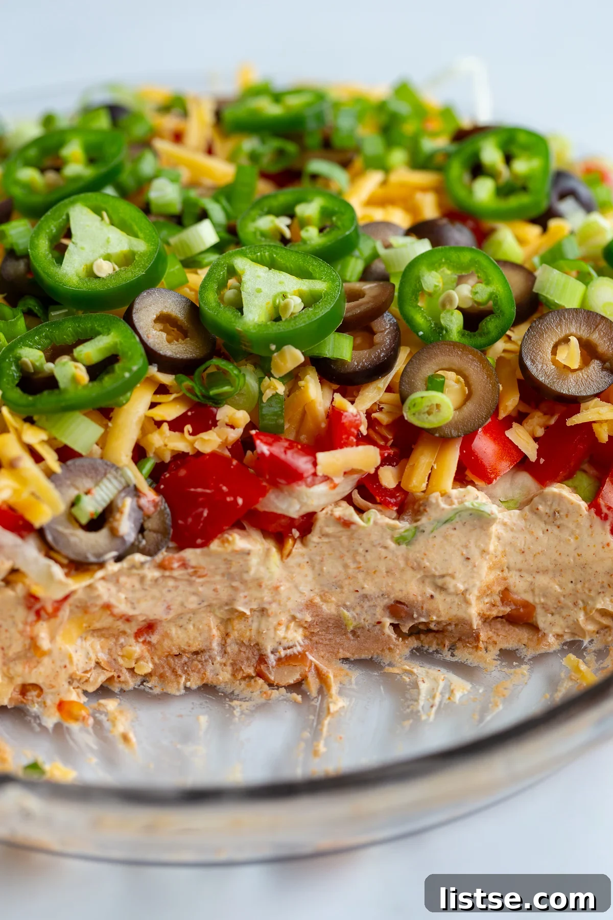 Cream Cheese Taco Dip Recipe for Parties 5 taco dip with cream cheese that's layered like a 7 layer dip with beans, cream cheese, lettuce, cheese, jalapeno, olives, and tomato. scoops are taken out so you can see the inside of the dip